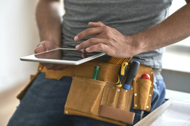 Close up of carpenter with tool belt scrolling digital tablet